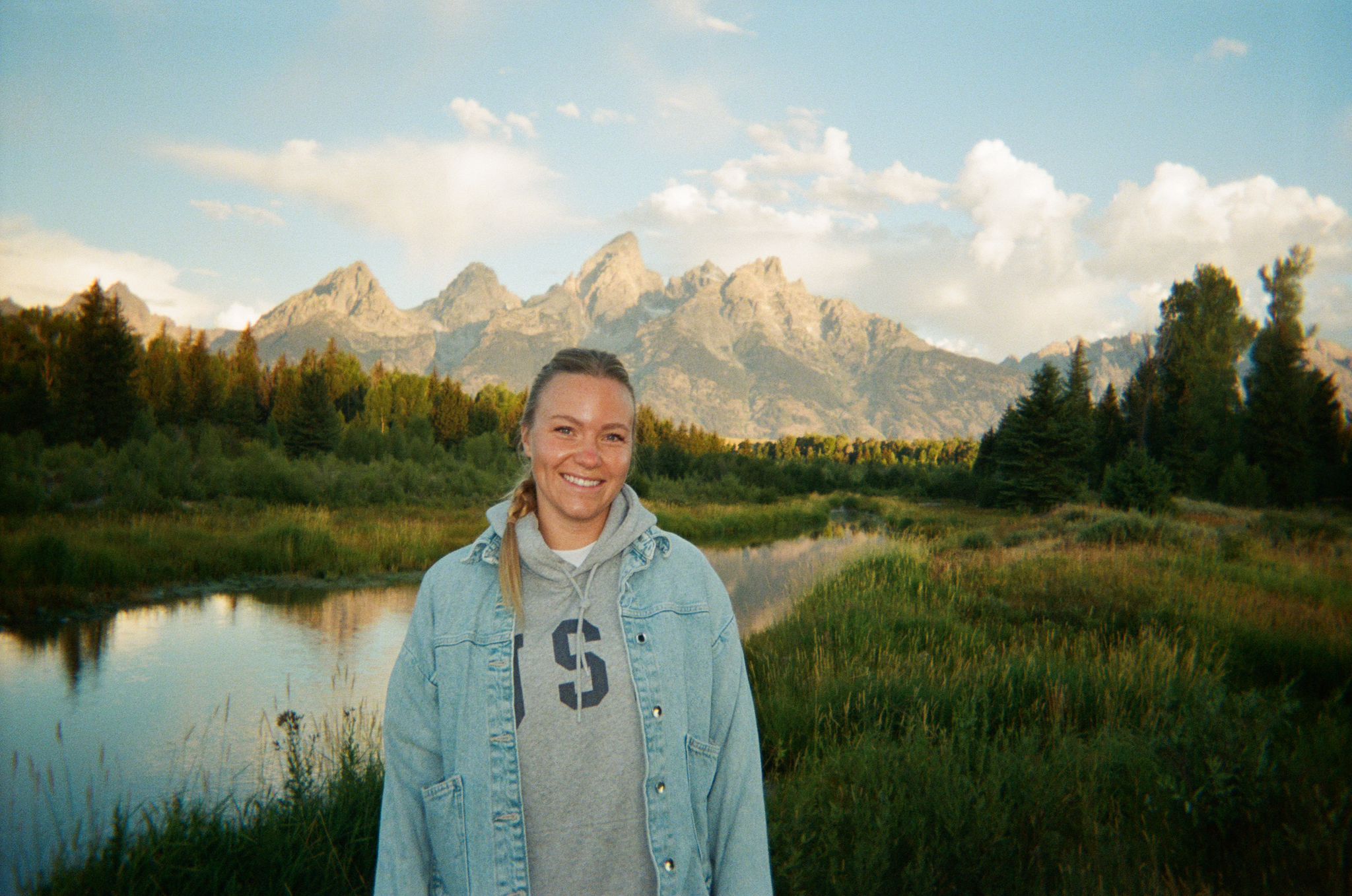 Aurelien smiling outdoors, mountains and a river behind her